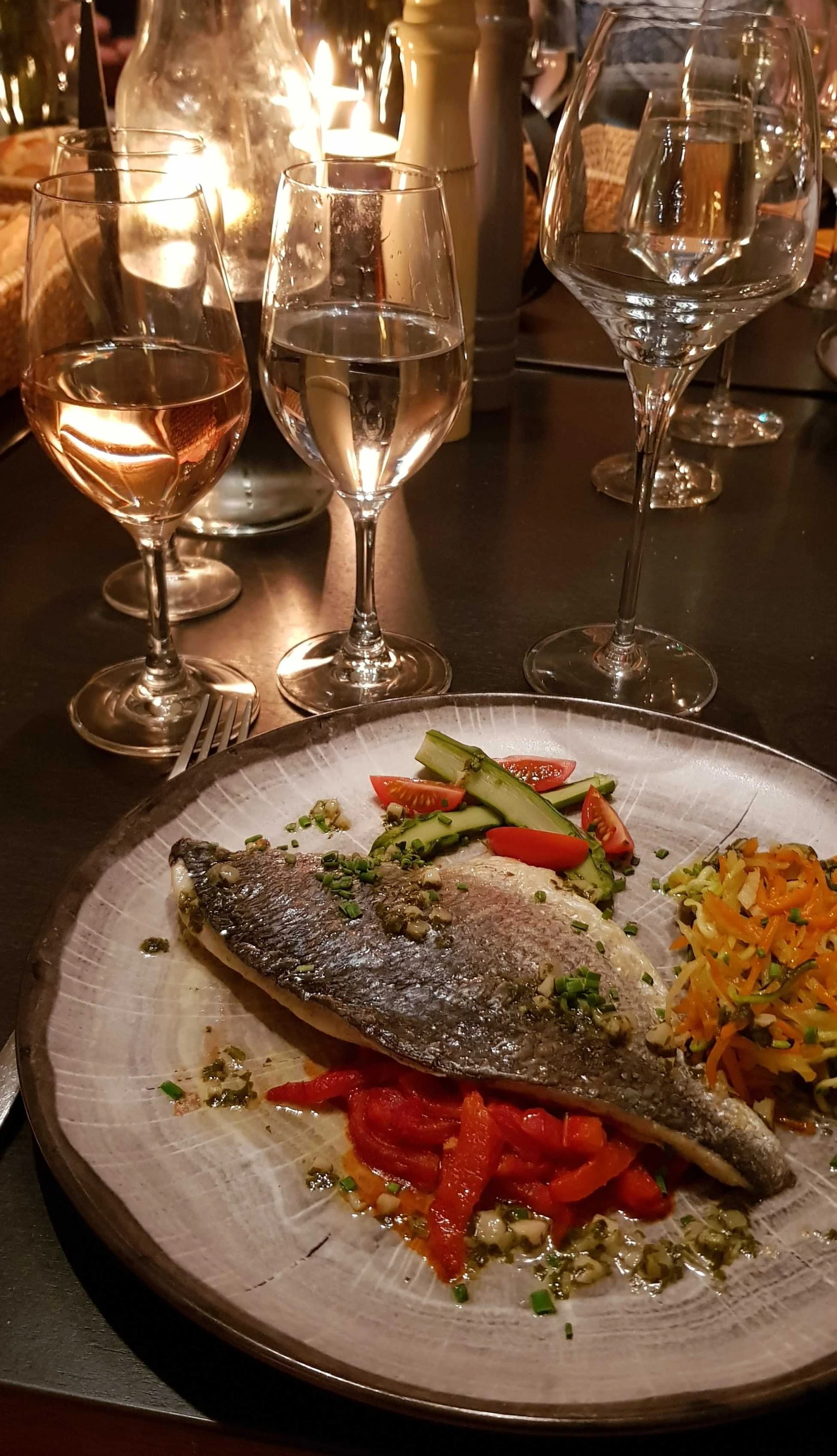 assiette avec poisson et vin blanc sur une table éclairée à l'aide d'une bougie