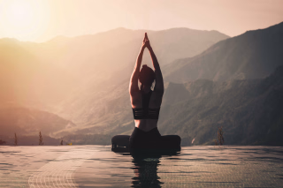 Femme assise au bord de l'eau au levé du soleil pour une séance de yoga