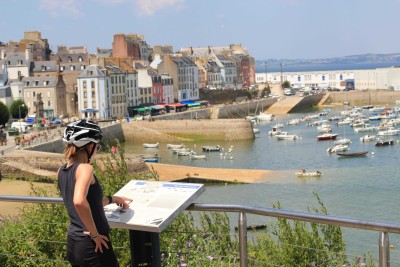 cycliste lisant un plan touristique face à un petit port breton