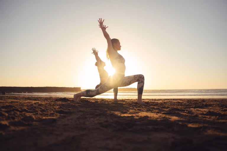 Deux personnes entrain de faire une séance de yoga au lever du soleil sur la plage